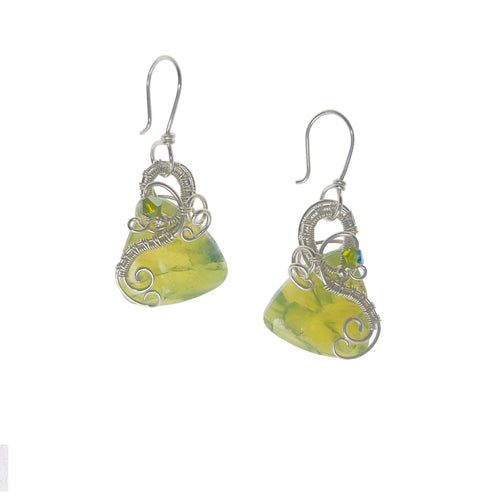 Dangle earrings with sterling silver loops and interlacing details curving down one side of a yellow-green triangle-shaped stone, accented by a vintage red Austrian crystal, a glass bead, and scrollwork.