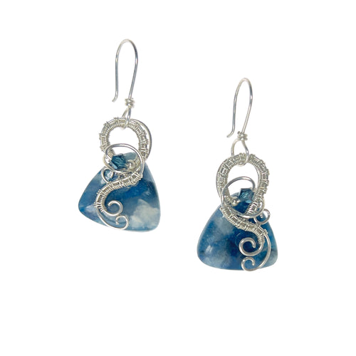 Dangle earrings with sterling silver loops and interlacing details curving down one side of a blue triangle-shaped stone, accented by a vintage blue Austrian crystal, a glass bead, and scrollwork.