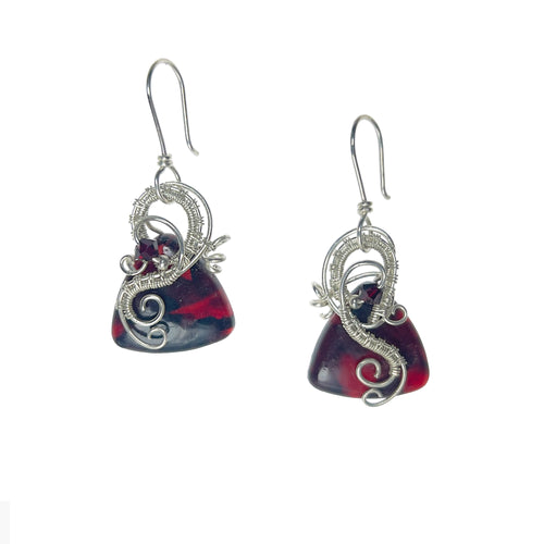 Dangle earrings with sterling silver loops and interlacing details curving down one side of a dark red triangle-shaped stone, accented by a vintage red Austrian crystal, a glass bead, and scrollwork.