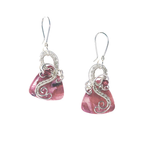 Dangle earrings with sterling silver loops and interlacing details curving down one side of a pink triangle-shaped stone, accented by a vintage red Austrian crystal, a glass bead, and scrollwork.