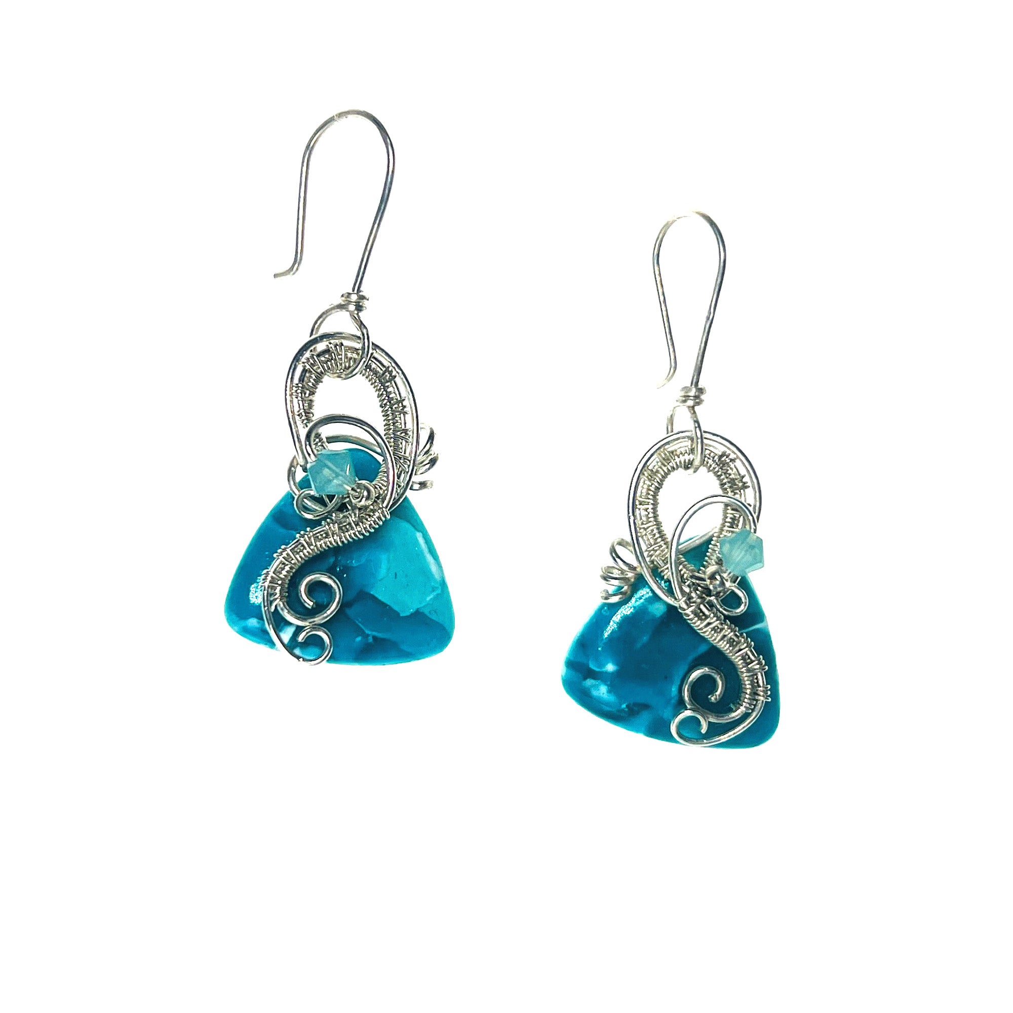 Dangle earrings with sterling silver loops and interlacing details curving down one side of a turquoise colored triangle-shaped stone, accented by a vintage red Austrian crystal, a glass bead, and scrollwork.