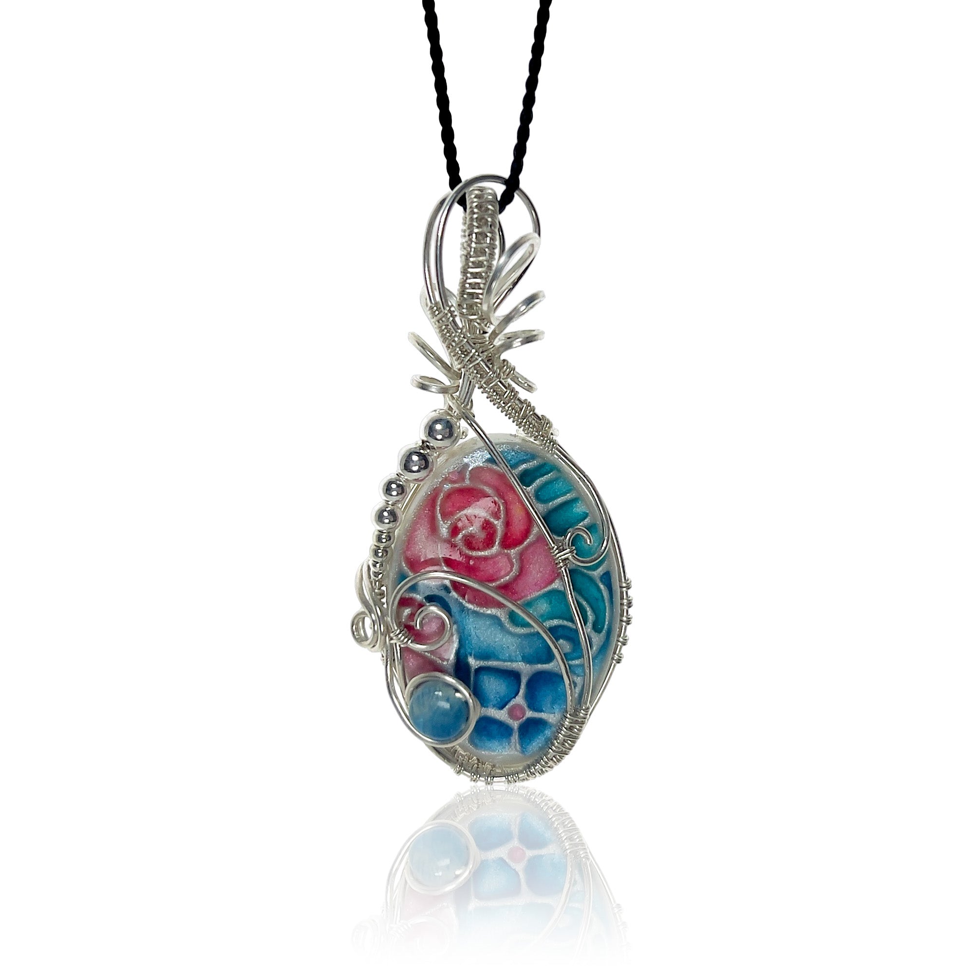Sterling silver scrollwork pendant necklace with a hand-painted floral design in pink, teal and blue, hung from a black silk cord.