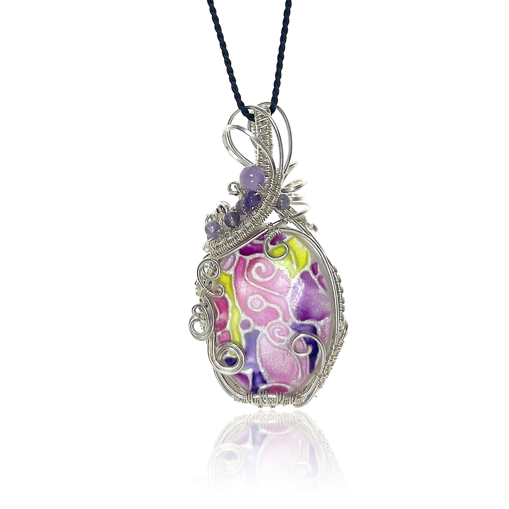 A pendant necklace featuring a floral design in pinks, purples, and peridots, with amethyst beads and sterling silver scrollwork on the left side;  suspended from a black cord on a white background.