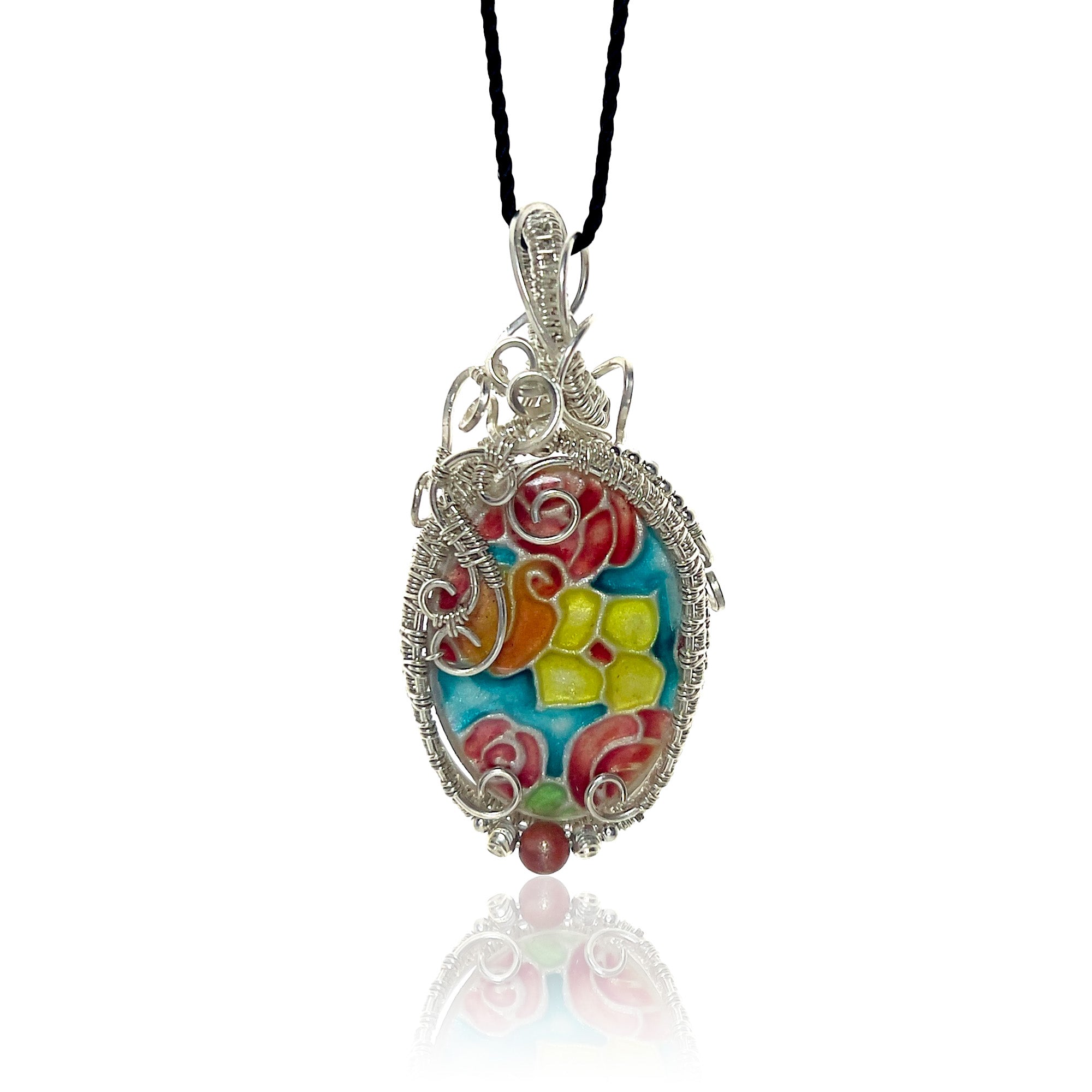 Sterling silver oval pendant necklace with interlaced wire detailing and hand-painted floral design in pink, orange, yellow, and blue, anchored by a matte red riverstone bead, hung from a black cord.