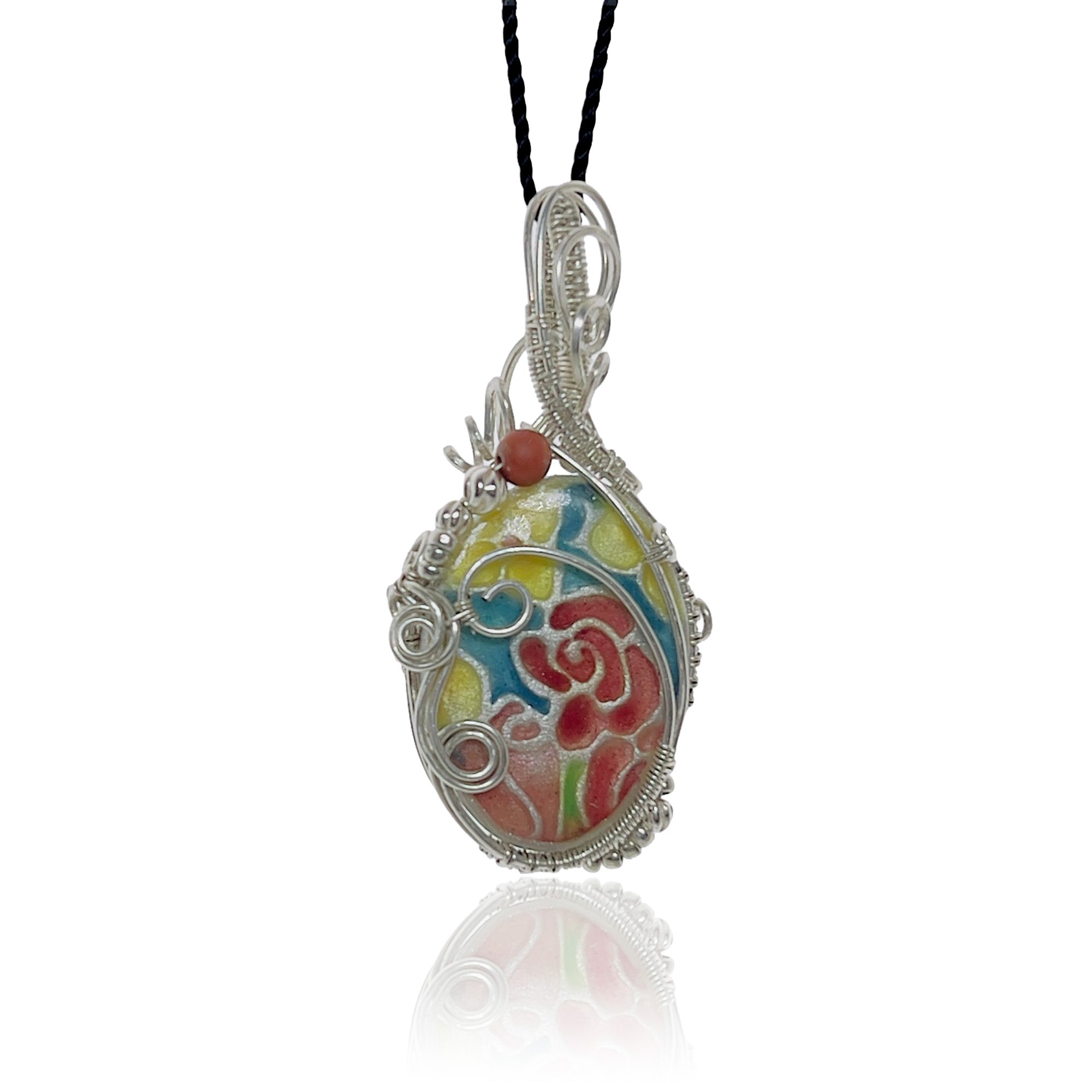 Sterling silver oval pendant necklace with a hand fabricated stone, hand-painted floral design in red, yellow, and blue, hung from a black cord.